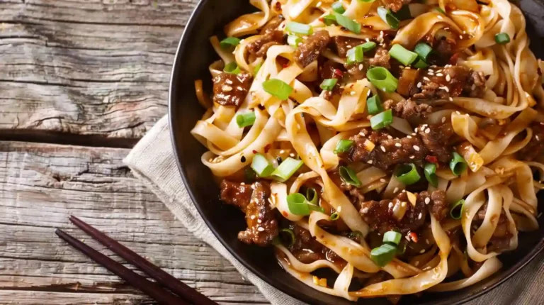 Mongolian ground beef noodles topped with scallions and sesame seeds in a dark bowl