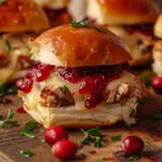 Close-up of a turkey cranberry slider with melted cheese and cranberry sauce on a golden bun.