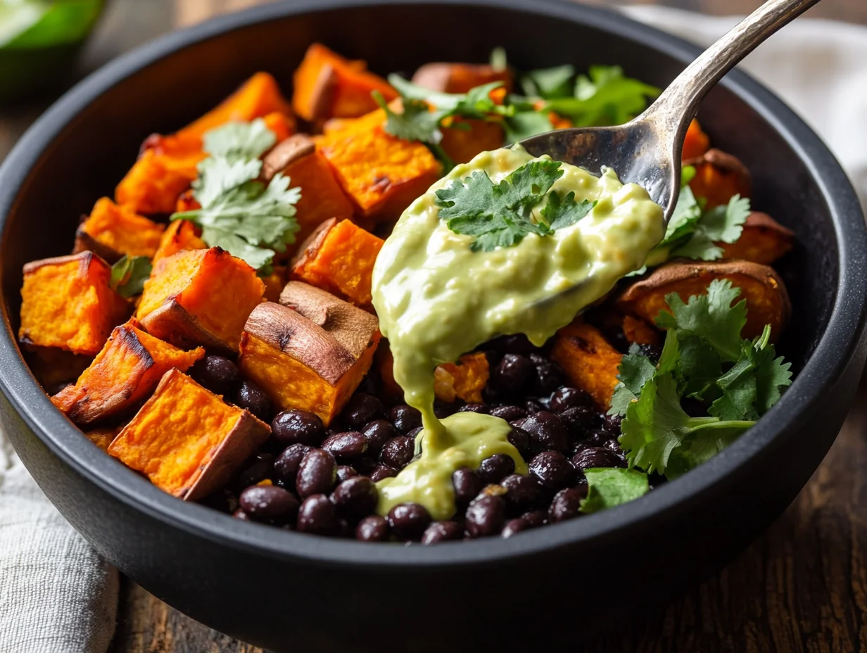 Sweet potato black bean power bowl with roasted cubes, black beans, quinoa, avocado and tahini dressing in white bowl